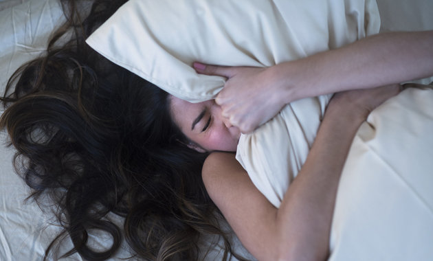 Frustrated Hispanic woman gripping pillow in bed