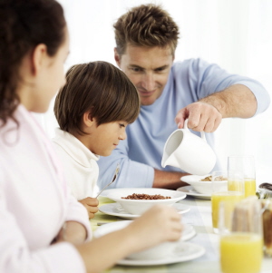 Young Father Pouring Milk into Bowl of Cereal for Young Boy (6-8) --- Image by ? Royalty-Free/Corbis