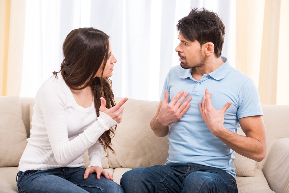 Portrait of frustrated couple are sitting on couch and are quarreling with each other.