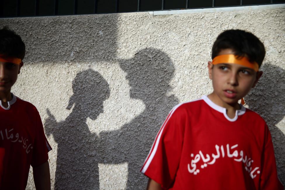 Boys stand near a shadow of a coach lecturing a boy during a final soccer game in a school championship, in the rebel held besieged town of Douma, eastern Damascus suburb of Ghouta