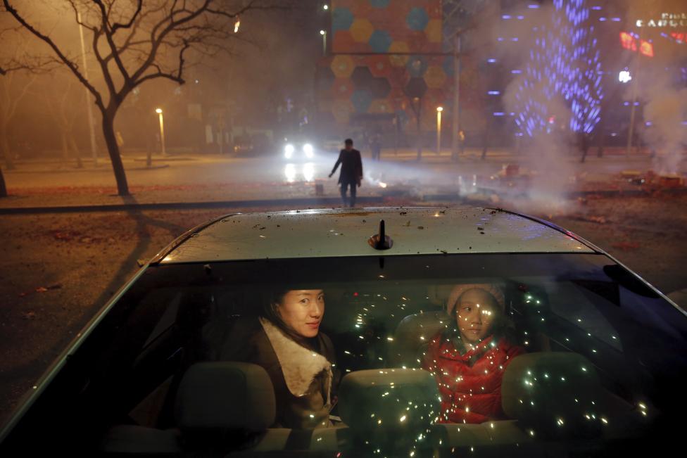 A girl and a woman sit inside the car as firecrackers and fireworks explode celebrating the start of the Chinese Lunar New Year of Monkey in Beijing