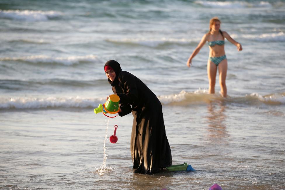 Muslim woman wearing a Hijab stands in the waters in the Mediterranean Sea as an Israeli stands nearby on the beach in Tel Aviv