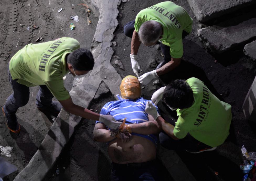 Funeral workers remove the masking tape wrapped around the head and the wrists of the body of a man, who police said is a victim of drug related vigilante execution in Manila