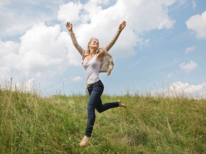 Young woman running through field with arms in air