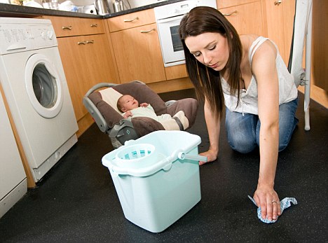 B1C9DM Woman cleaning floor with baby in background