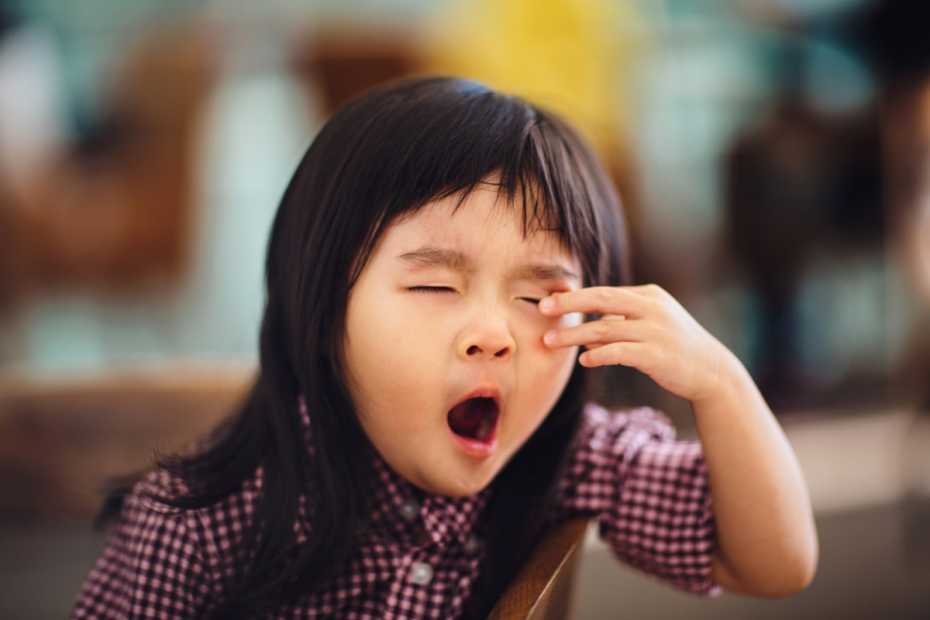 Toddler girl yawning & rubbing eyes in cafe