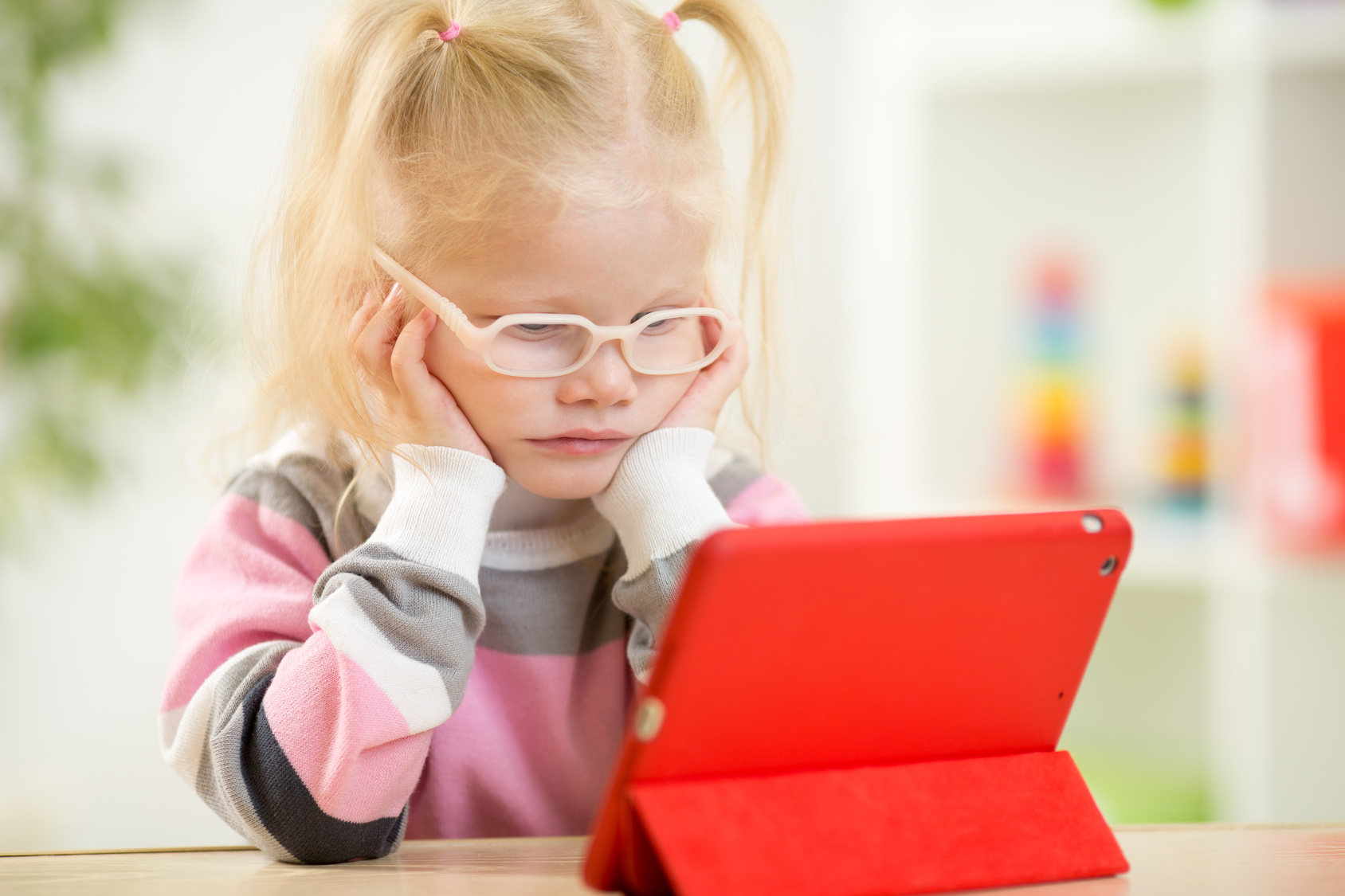 happy child in glasses looking at mini tablet pc screen sitting at table