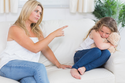 Angry mother scolding daughter clutchin teddy bear in living room