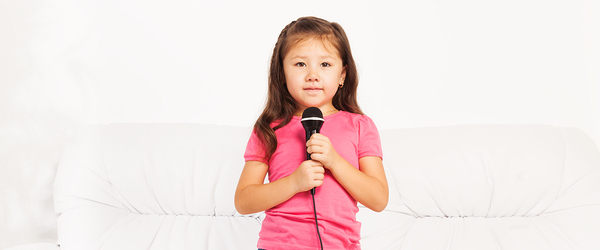 Cute little Asian five years old girl with dark long hair singing to microphone performing standing in living room