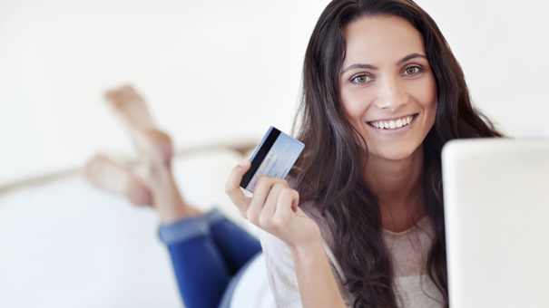 Portrait of a young woman holding a credit card while using a laptop