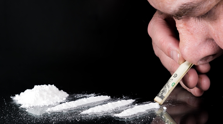 Man snorting a line of cocaine through a rolled up bill. There are three lines of cocaine, and a small pile. The table is black glass. focus is on the end of the bill. There is room for text.