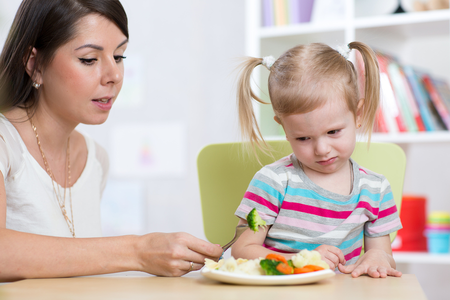Child girl looks with disgust at healthy vegetables. Mother conv