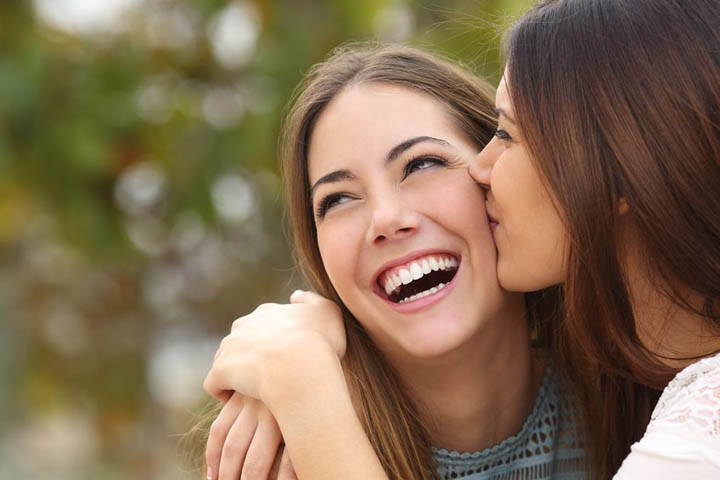 35933763 - woman laughing with perfect teeth while a friend is kissing her with a green background