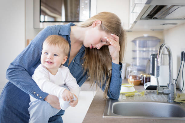 Tired mom with baby in her arms standing by the sink