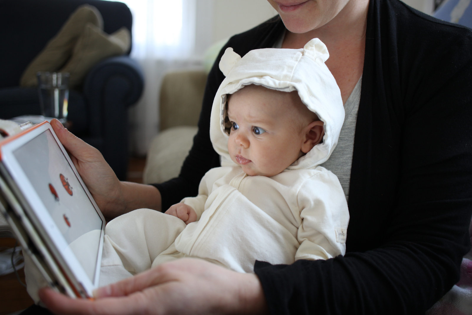 A two month old baby girl watches an interactive app for babies on an iPad while held by her mother.