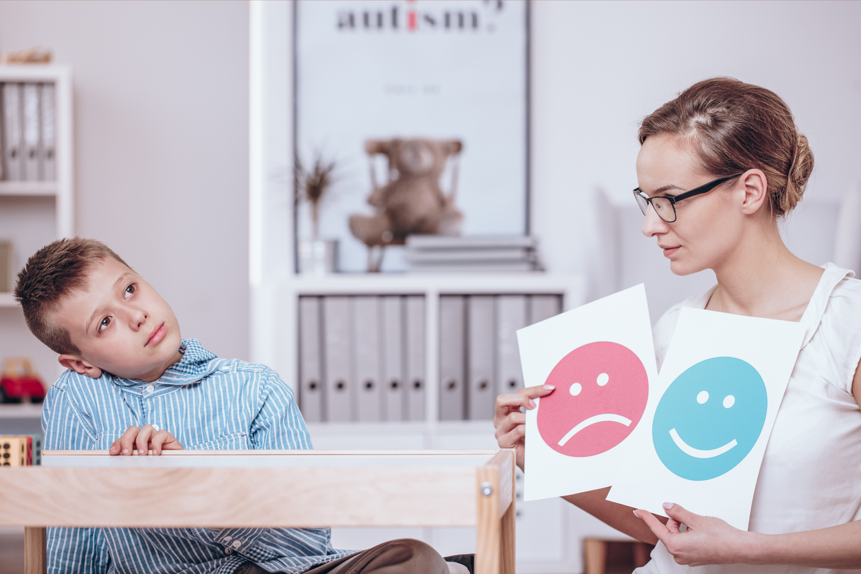 Counselor with posters of red and blue icons teaching autistic kid of good and bad behaviors