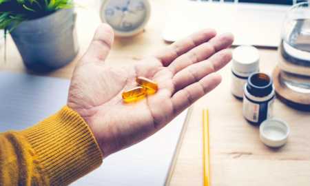 person-at-desk-holding-omega-3-supplements-in-palm